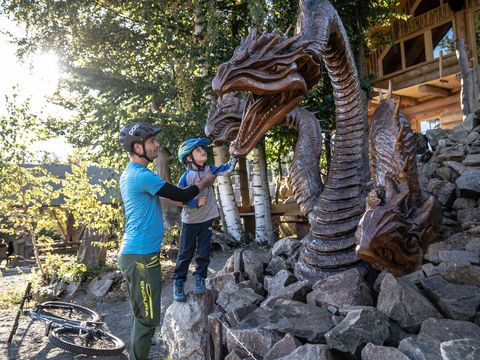 Ein Vater steht mit seinem Sohn vor einem aus Holz gesägten Drachen.