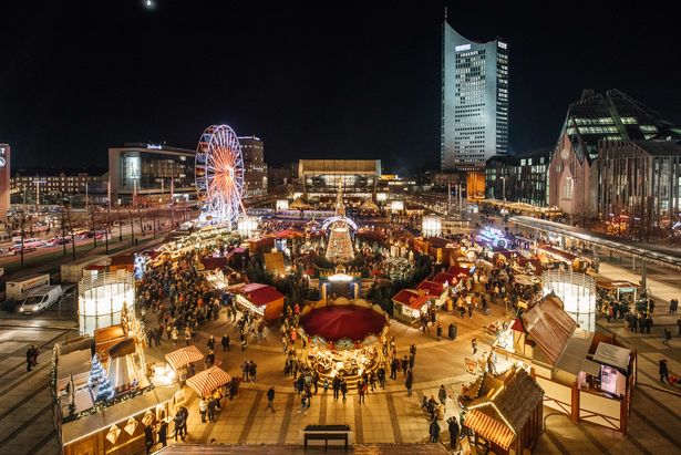 Aus der Vogelperspektive sieht man den Weihnachtsmarkt auf dem Augustusplatz in Leipzig. Im Hintergrund ist ein Hochhaus zu sehen, welches an ein aufgeklapptes Buch erinnert. Der Weihnachtsmarkt ist mit Lichterglanz gesäumt. Es herrscht Abendstimmung.