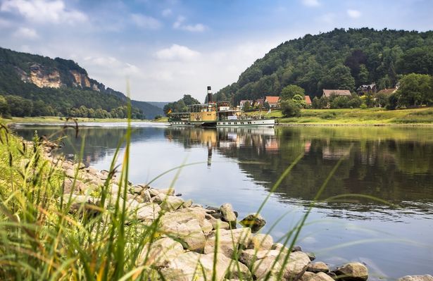 Auf der Elbe fährt ein Schaufelraddampfer. Links und rechts erheben sich die Felsen der Sächsischen Schweiz.